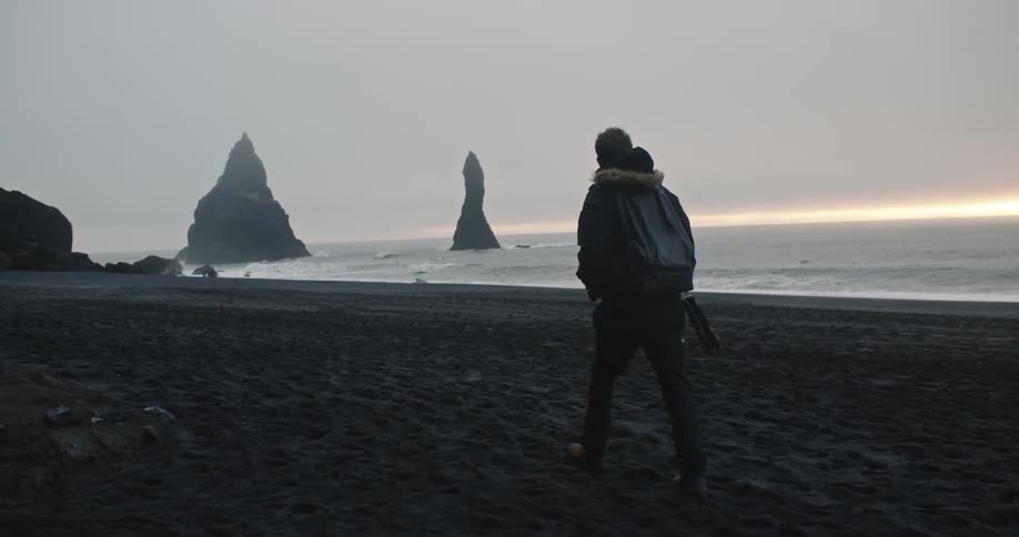 Young man walking on the reynisfjara black sand beach at sunset
