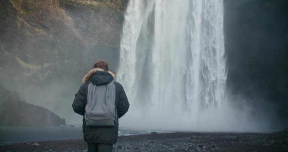 A man is walking towards the waterfall