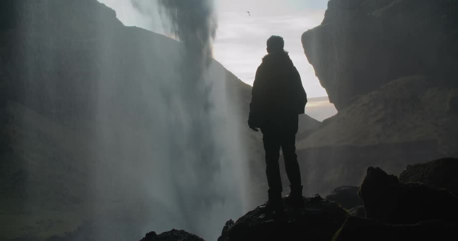 A man is standing outdoors and watching a waterfall