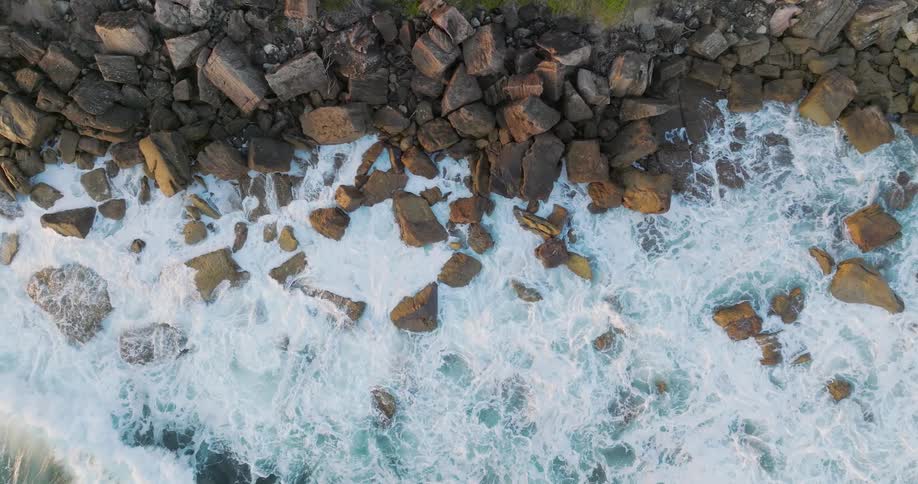 Aerial view of ocean waves gently washing over the rocks in the coast at sunset