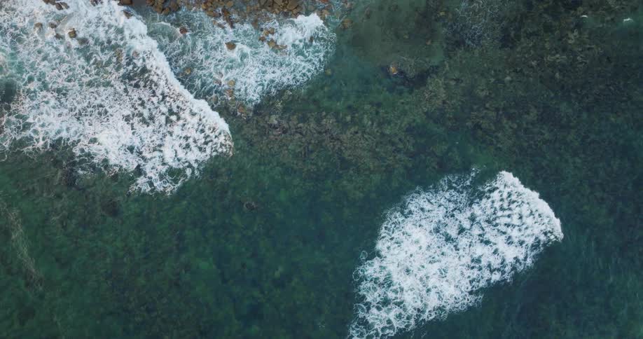 Birds eye view of waves breaking over reefs in the ocean in slow motion