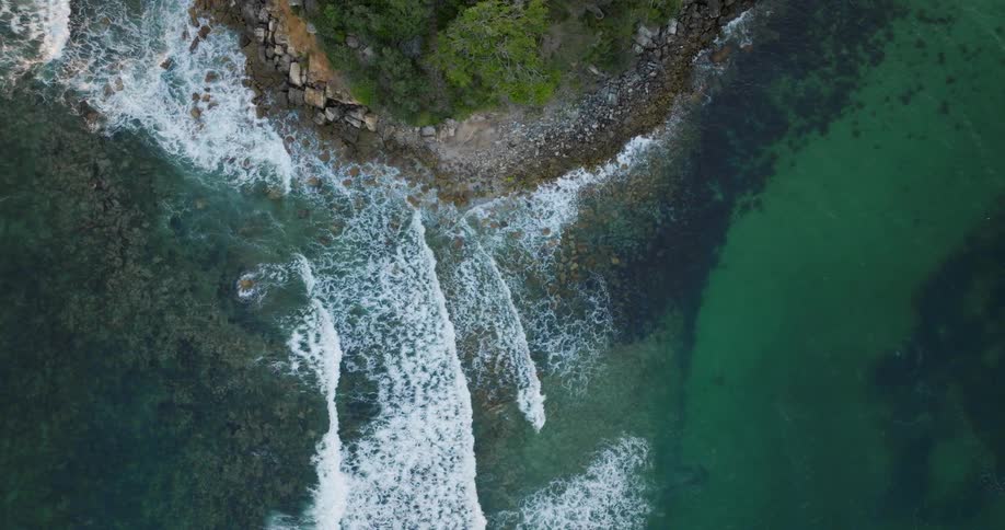 Aerial view of a clear water coastline as waves roll on the shore