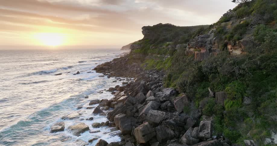Waves roll over a rocky shoreline as the sun shines on the horizon