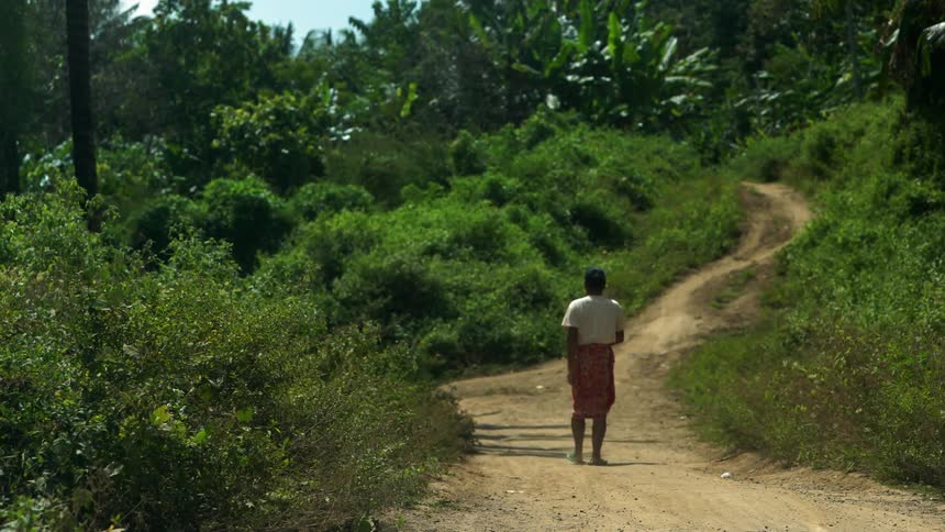 A villager walks down a dirt trail on a sunny day