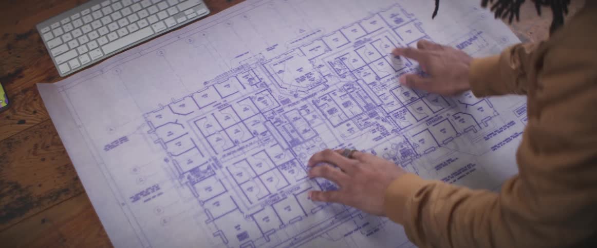 Man working at the office unrolls a blueprint over a wooden desk