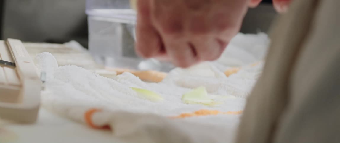 Person with apron around their waist peels vegetable with a knife