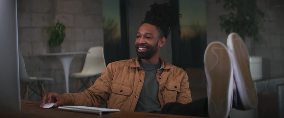 A man sitting at his desk with his feet up smiling at the monitor