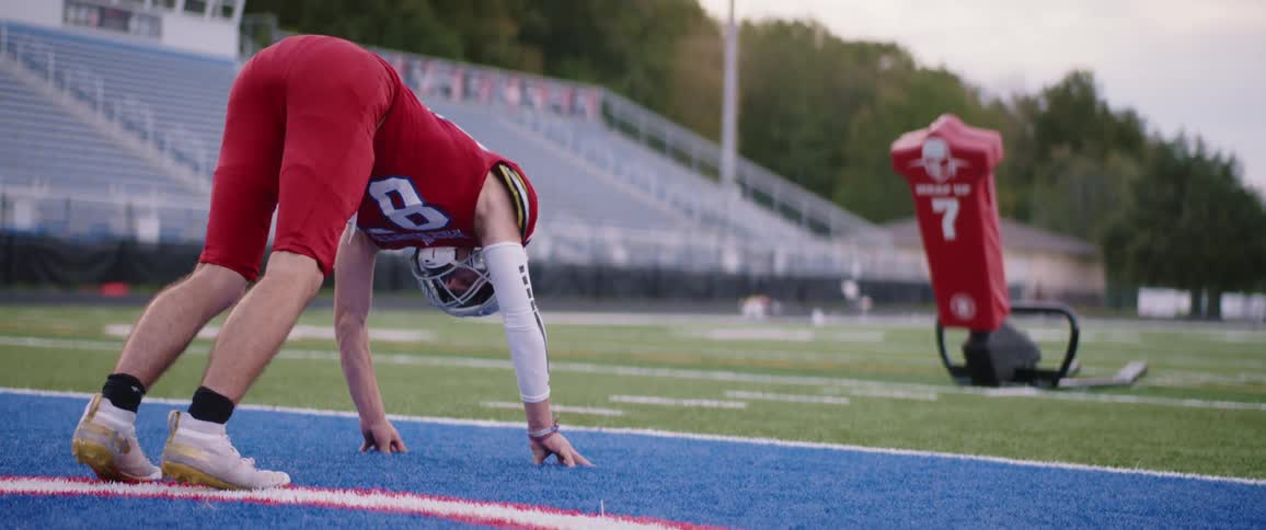 Young footgball player wearing a red uniform stretching in front of a dummy in a stadium