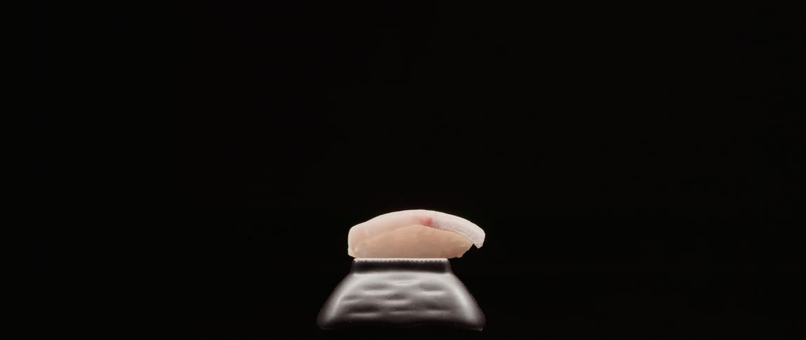 A person serves a piece of sushi with chopsticks
