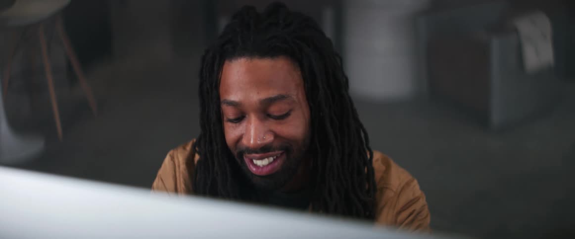 Young bearded man with long hair smiles while using a computer