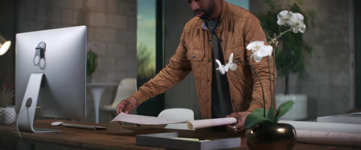 Man stands near desk looking at blueprint as setting sunlight shines through window