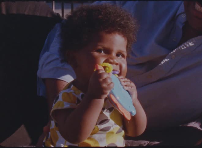 Toddler chewing on a toy next to her father over the grass in the porch at morning
