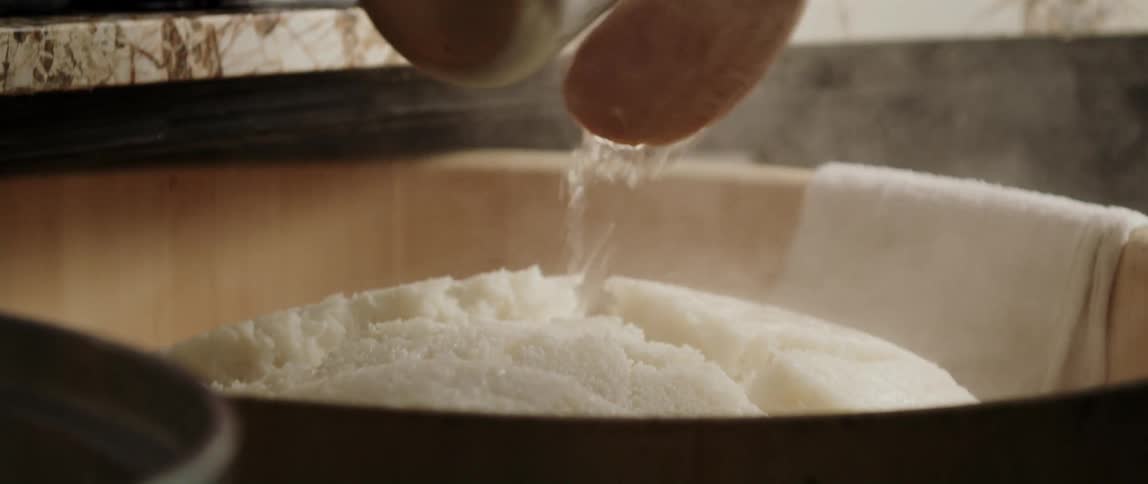Chef pours water over a big steaming ball of cooked sushi rice on a restaurant