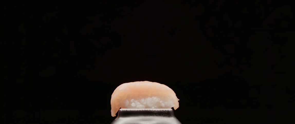 A piece of sushi sitting on a stand against a black background