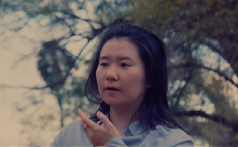 Woman smells the palm of her hand while standing near the trees outdoors caught on vintage film