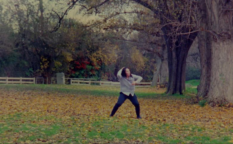 A teenage girl is outside dancing in a yard full of fall colored leaves