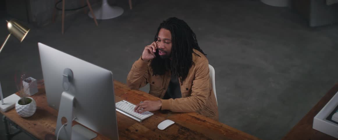 A man laughs while talking on the phone and using his computer