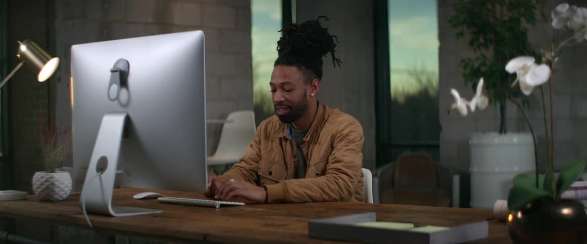 A man is sitting at a desk smiling as he types on a computer keyboard