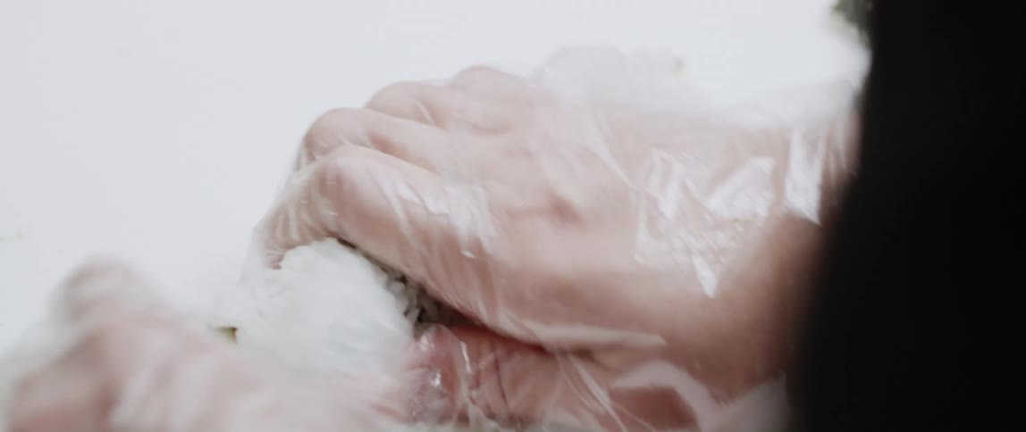 A person wearing plastic gloves is making a sushi roll