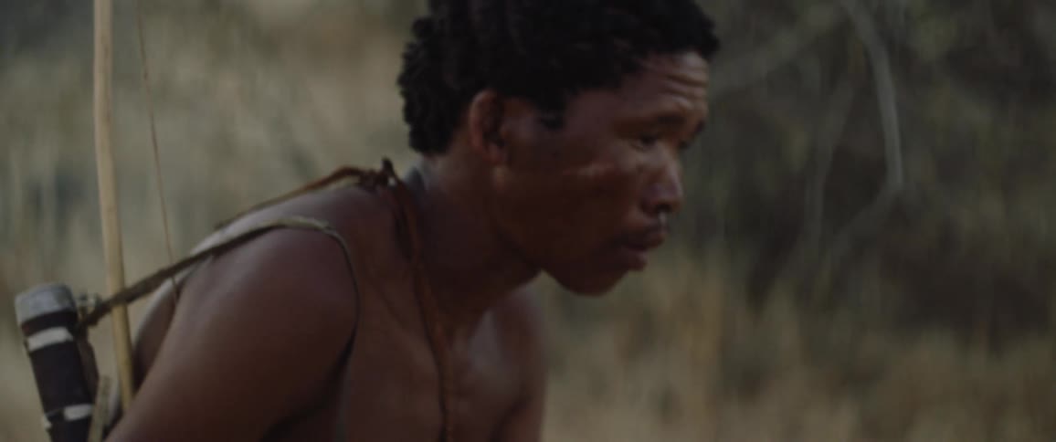 Tribal men walks through a field with a bow and arrow