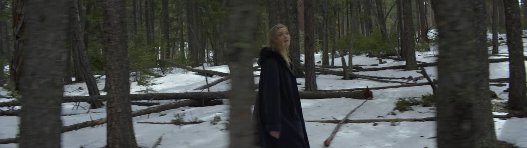 A teenage girl walks through a forest looking all around her as though she is lost