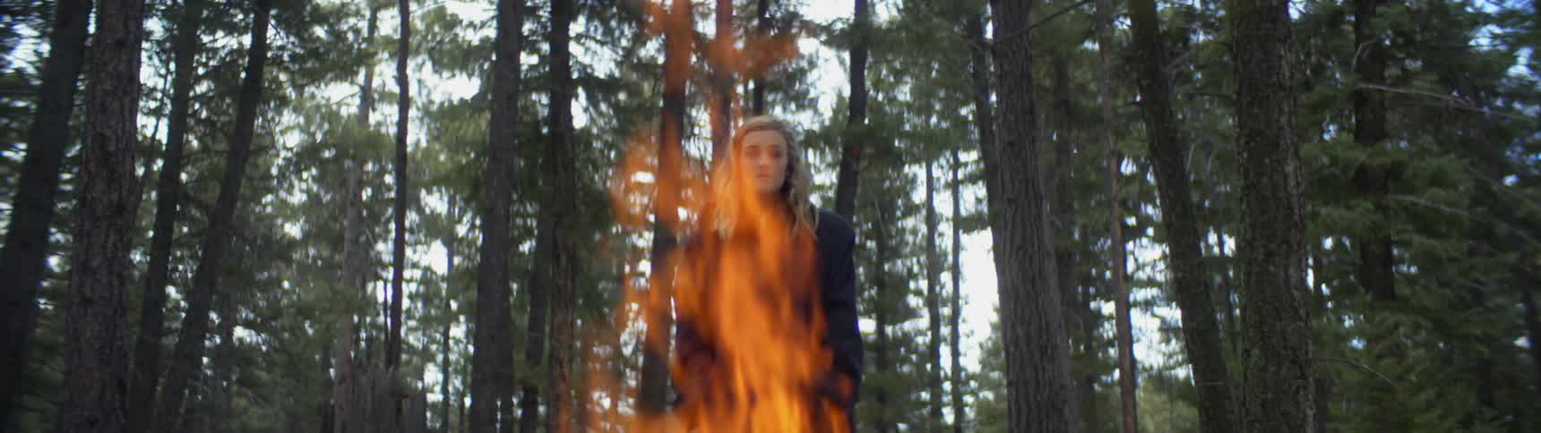 A woman is standing by a bonfire in the forest