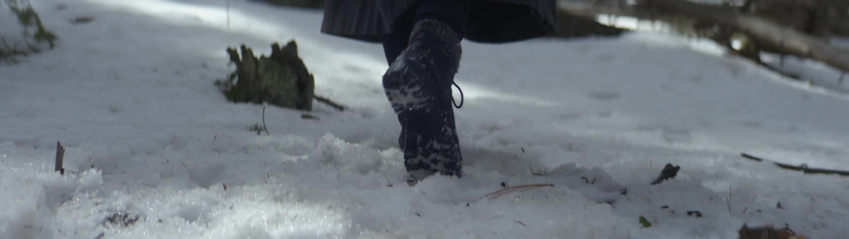 Someone wearing boots and a long coat is walking through the snow