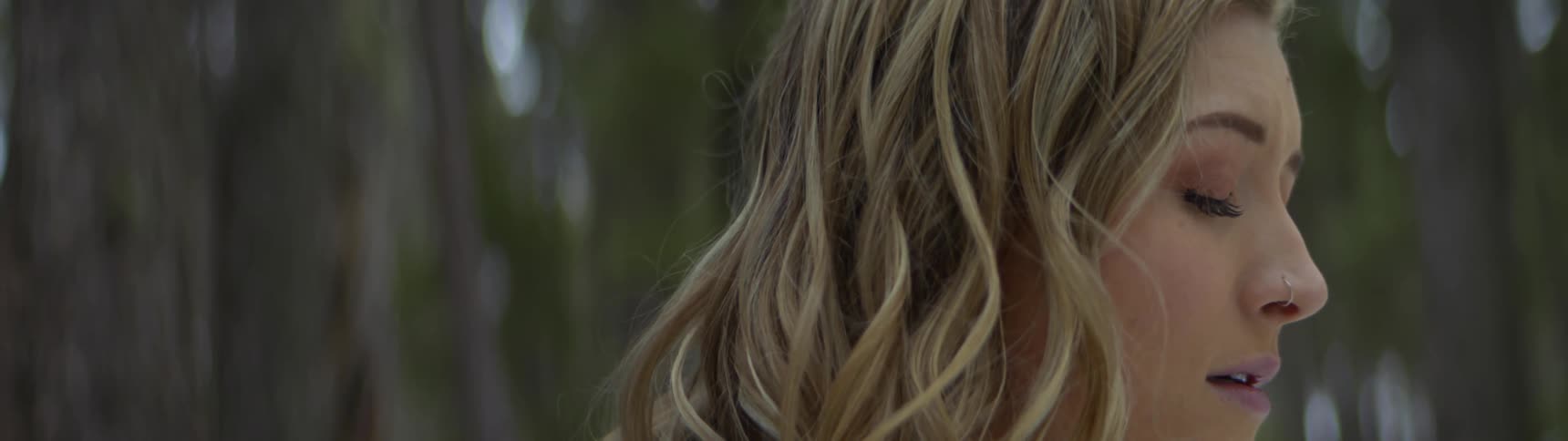 Blonde woman in the woods looks up then closes her eyes