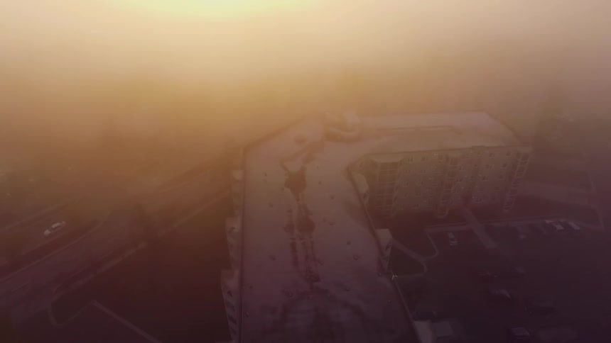 Heavy fog clears showing the rooftop of an apartment building with parking lot and a highway next to it