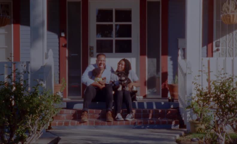 A man and woman sitting on the front steps of their home with dad holding baby and mom holding a puppy