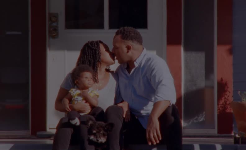Parents kiss as they sit on front porch steps with child and dog