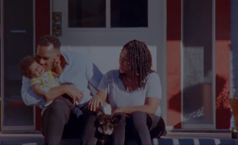 Mother smiles as father hugs and kisses baby while they sit on the porch steps