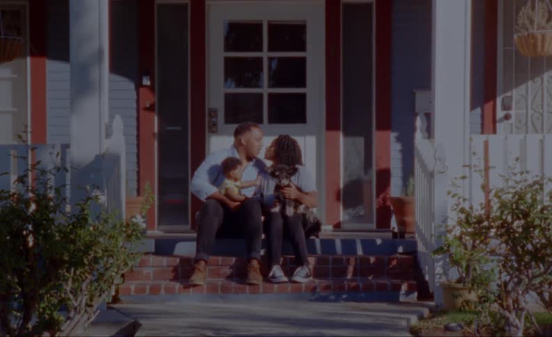 Parents sitting on front porch with child and dog share a kiss