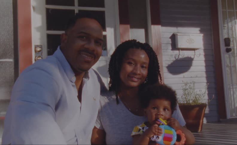 A husband and wife pose with their baby daughter for a photo on the front step of a house