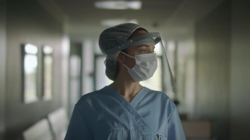 Nurse wearing face mask and shield walks along corridor