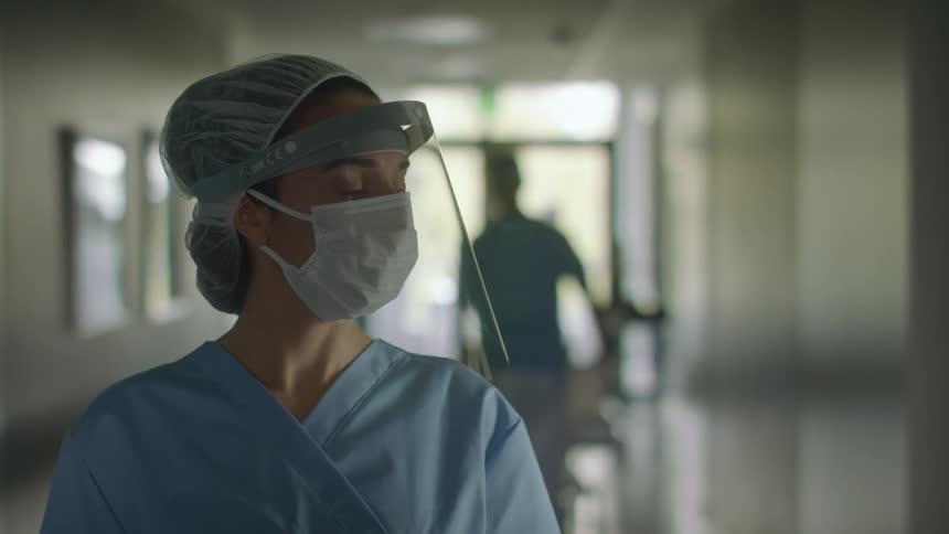 A nurse stops and looks around while walking down a hallway