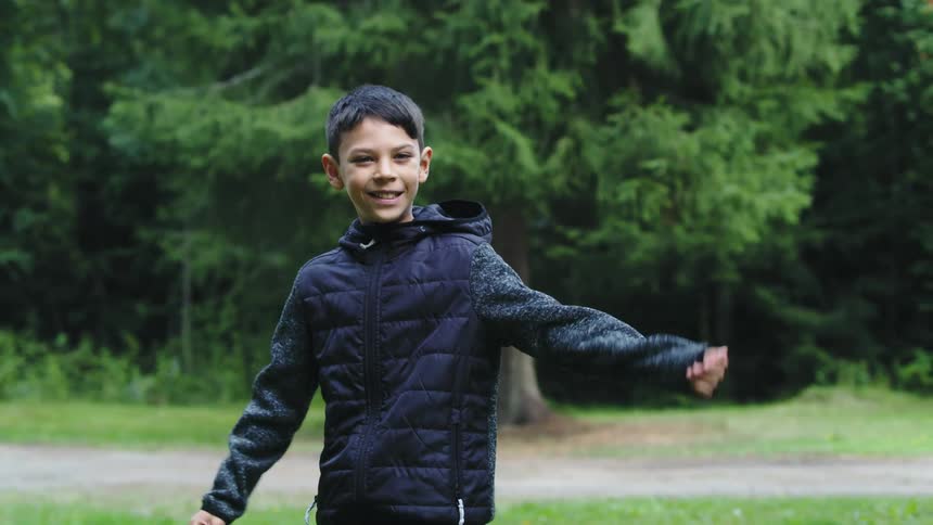 A young boy dances near a trail in a park