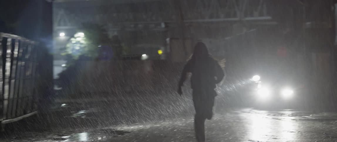 A person races down a street in the rain being chased by a police car