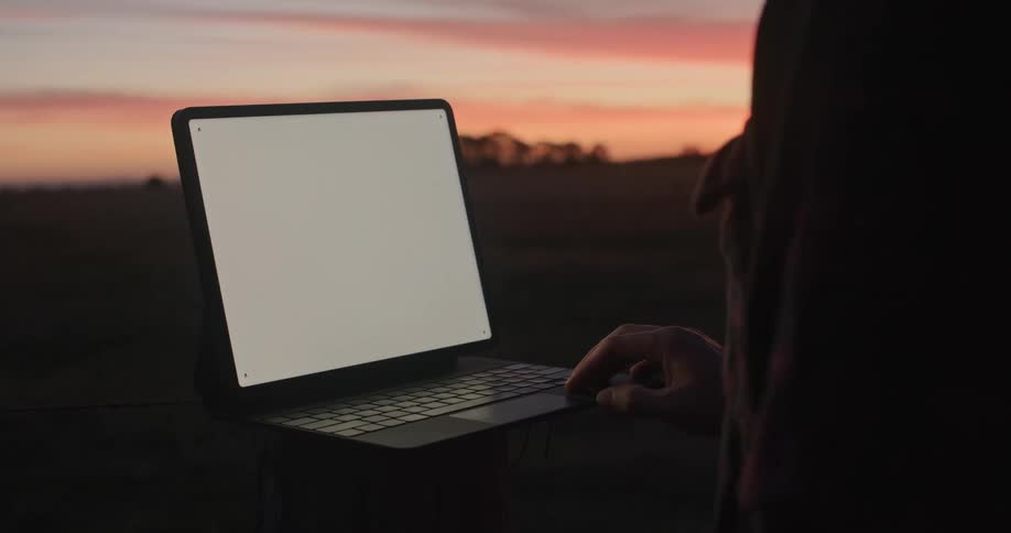 A man in a field stands in front of a laptop with a white screen
