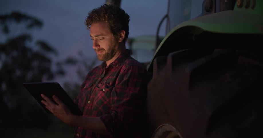 A man leans against a shipping truck and uses a tablet