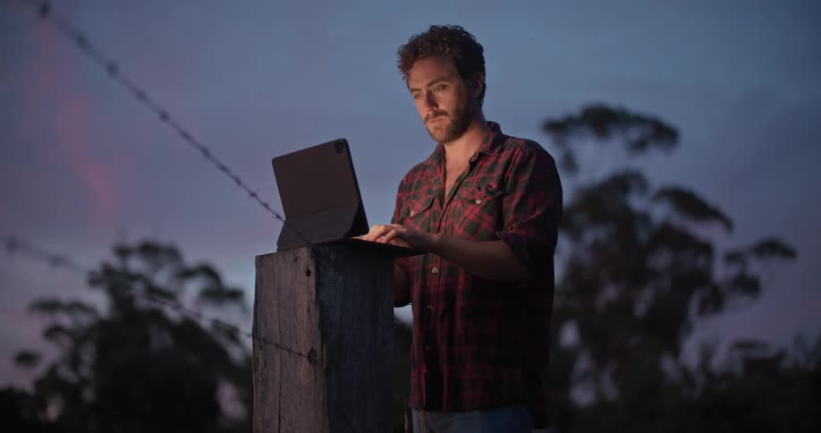 A man is typing on his tablet outside