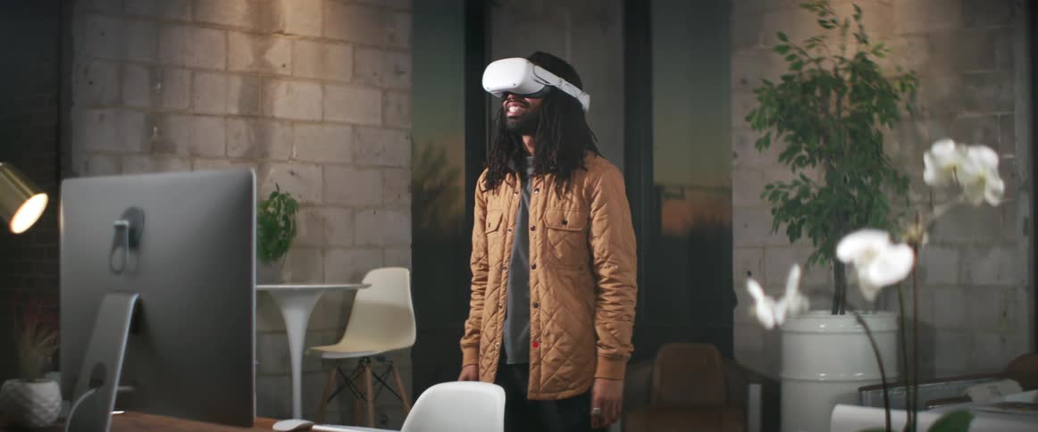 A man stands in front of a computer at home and puts on virtual reality goggles
