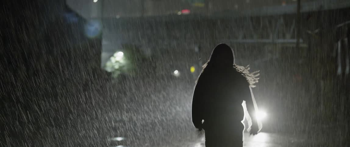 A person is running from a vehicle in the rain at night