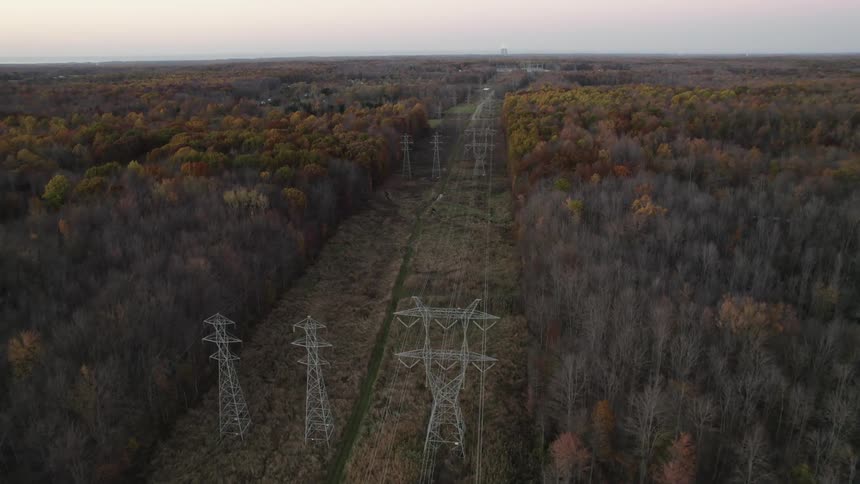Aerial view of transmission towers on a corridor through the forest at morning