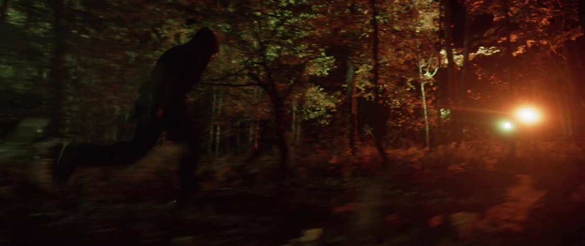 A man is running quickly through a forest with spotlights following him