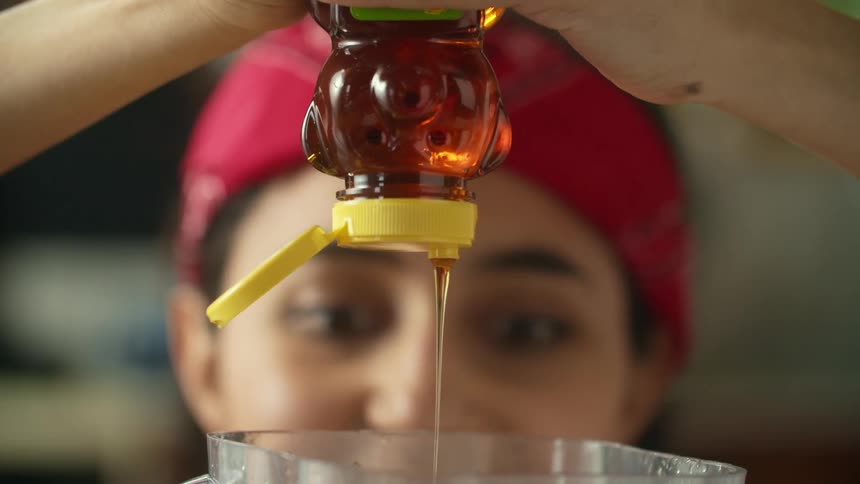 Young woman wearing a red bandana on her head pouring honey inside a blender