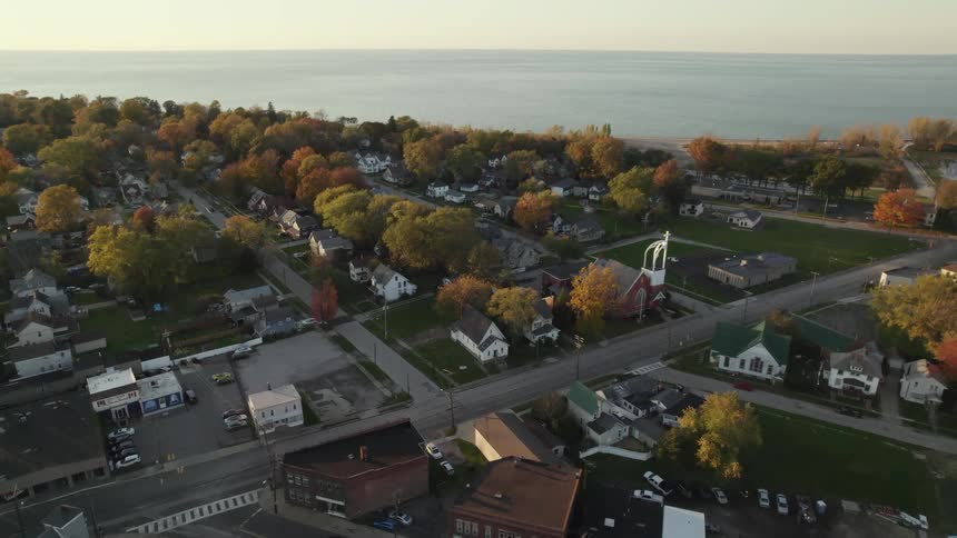 An aerial view of a neighborhood with cars parked and driving and the water in the distance