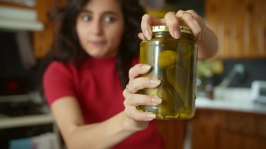 A woman is trying to open a jar of pickels