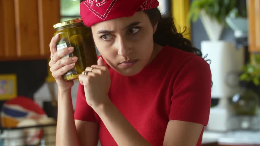A woman is holding a jar of pickles in her kitchen