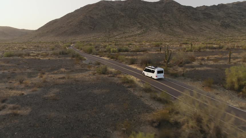 Aerial view of a white passenger van travelling on a road through the badlands at sunset